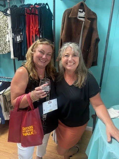 Camas Art and Wine Walk volunteers holding event-branded tote bags and glassware inside a local boutique.