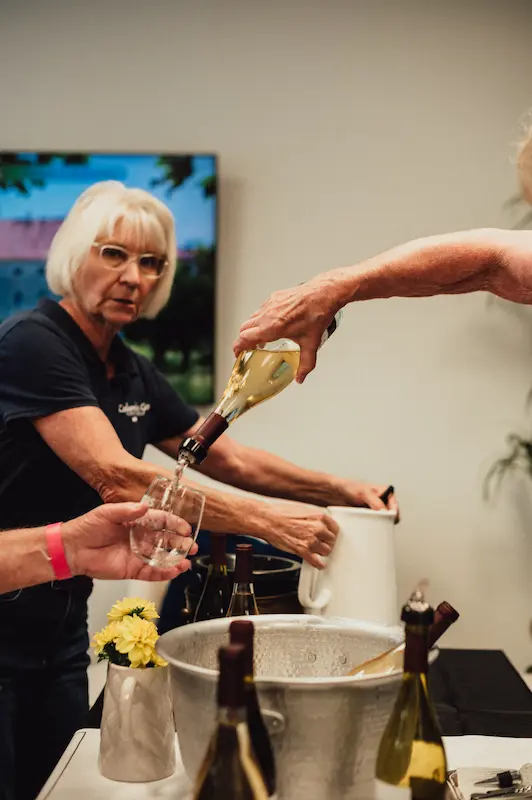 A wine pourer serving white wine to an attendee at a tasting station during the Camas Art and Wine Walk.