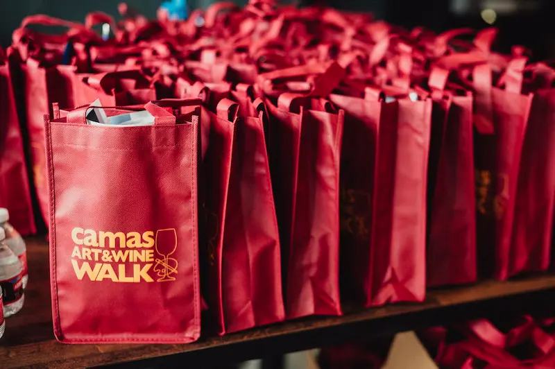 Rows of red Camas Art and Wine Walk reusable bags prepared for event attendees in Camas, Washington.