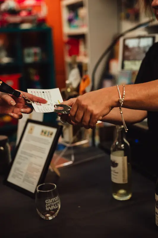 Close-up of an event staff member punching an attendee's official Camas Art and Wine Walk tasting card.