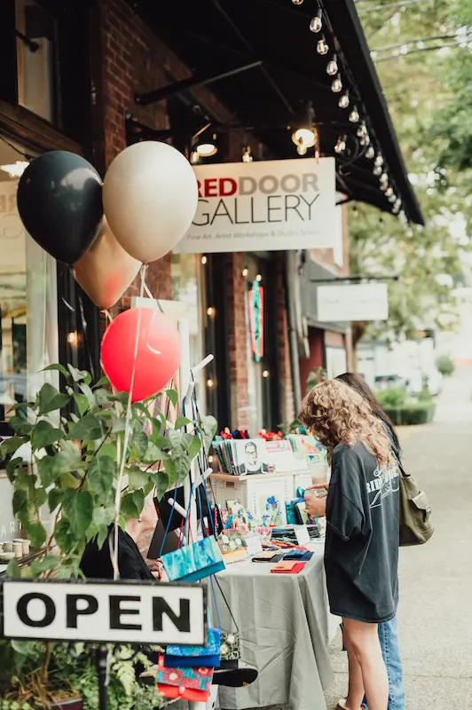 Visitors browsing an outdoor vendor table in front of the Red Door Gallery in Downtown Camas, Washington.
