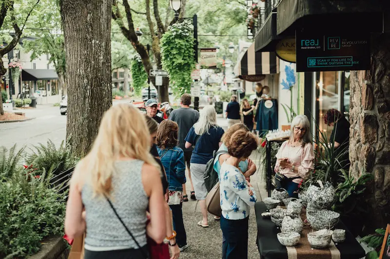 Crowds of visitors exploring outdoor art displays and local shops along the sidewalks of Downtown Camas, Washington.