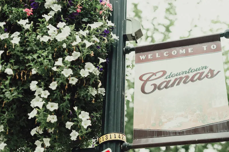 A "Welcome to Downtown Camas" street sign surrounded by flowers, signaling the location of the Art and Wine Walk.