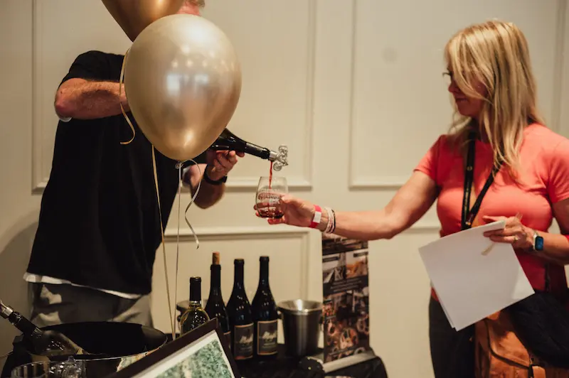 Red wine being poured for a guest at a balloon decorated tasting booth during the Camas Art and Wine Walk community event.